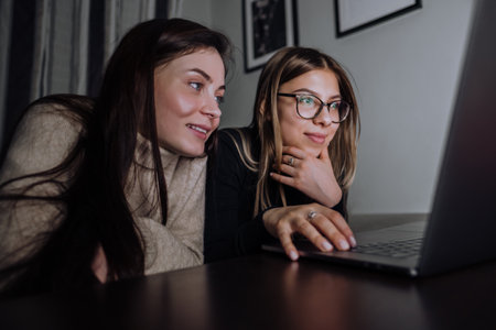 Two young girls lying on a sofa and looking at the laptop screen, typing text.の写真素材