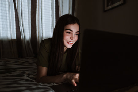 Smiling young european woman lying on sofa at home, working distantly on computer. chatting with friends in social networks, studying online, surfing information.の写真素材