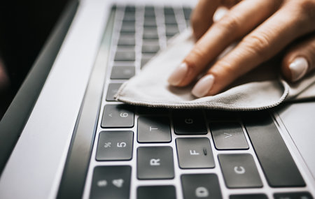 Care for computer equipment, woman hand wipes laptop keyboard from dust. High quality photo