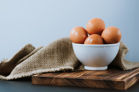 Chicken eggs in a white bowl on a wooden board. Top view.の写真素材