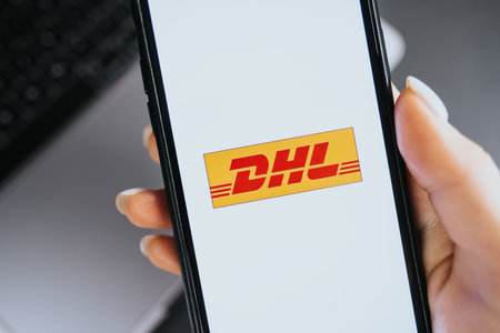 Hand holding iPhone X with DHL logo on the screen. DHL is a popular delivery company.のeditorial素材