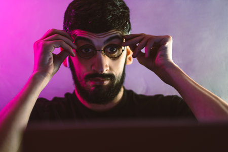Shocked young man with glasses looking at a laptop in a room with colored lighting. High quality photo.の写真素材