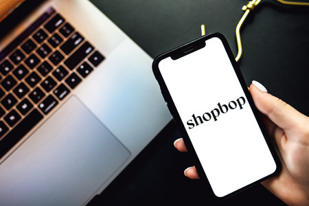 Hands holding the iPhone X with shopbop app logo on the screen. Shopbop is a fashion clothing online store.のeditorial素材