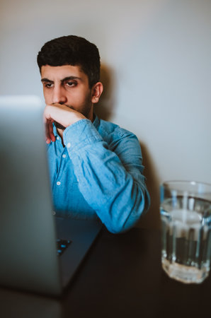 Close-up of a man working on a laptop, sitting at a wooden table. Chatting with friends in social networks, studying online, surfing information.の写真素材