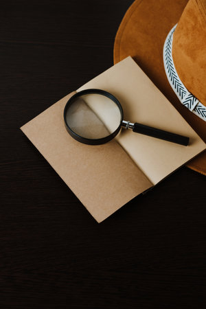 Notebook with craft paper and a magnifying glass on a black wooden background with copy space.の写真素材