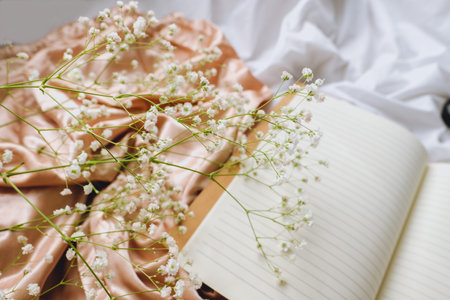 Spring composition, white gypsophila flowers with notebook and magnifying glass on the gold satin fabric.の写真素材