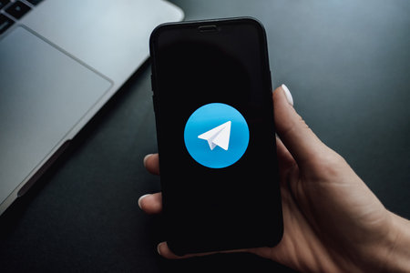 Womans hand holding iPhone X with telegram private messenger app.