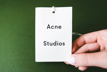 Closeup of Acne Studios logo label on green background. Acne Studios is fashion clothing store.のeditorial素材