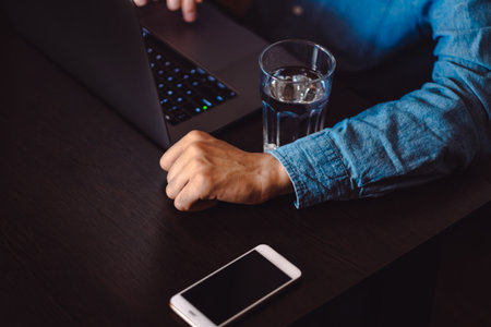 Close-up of a man working on a laptop, sitting at a wooden table. Chatting with friends in social networks, studying online, surfing information.の写真素材