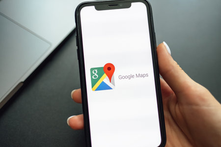 Hands holding the iPhone X with google maps app logo on the screen. Top view.のeditorial素材