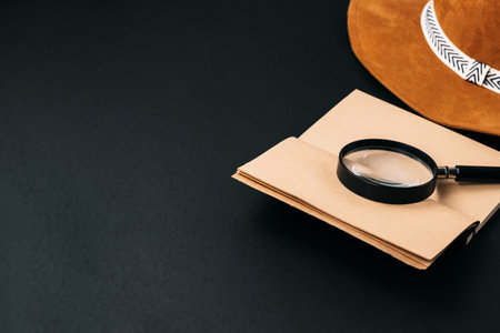 Notebook with craft paper and a magnifying glass on a black background with copy space. High quality photoの写真素材
