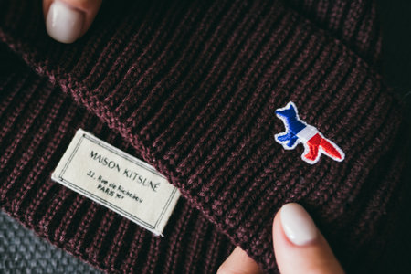 Closeup of Maison Kitsune logo label on green background. Maison Kitsune is fashion clothing store.