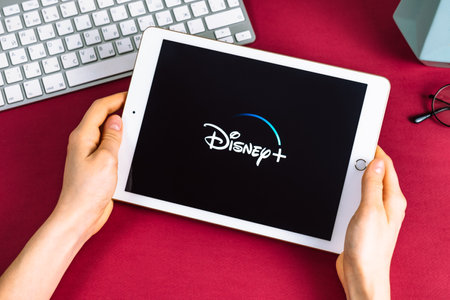 Girl holding a tablet with Disney plus logo on the screen. High quality photo.