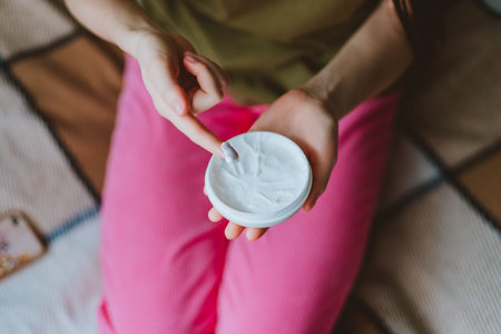 Young female uses body cream while sitting at home on the bed.の写真素材
