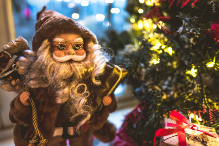 Santa Claus toy near Christmas tree with gifts on a widow. Christmas background.