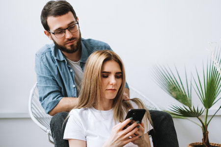 Husband looking as wife uses smartphone. High quality photo