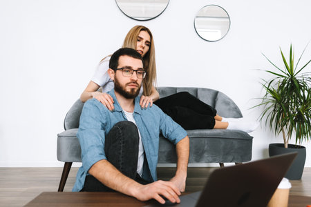 Young couple using laptop computer, browsing information and looking at laptop screen in modern...