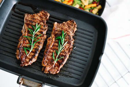 Grilled beef steak with rosemary in black grill pan on the table. High quality photoの写真素材