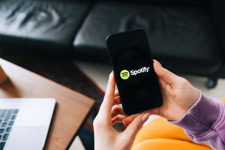 Hand holding iPhone with Spotify app logo on the screenのeditorial素材