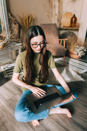 Young caucasian woman work on laptop computer looking on display, sitting on floor at home.の写真素材
