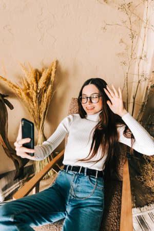 Young caucasian woman using video call on mobile phone at home, weaving. Chatting with family or...