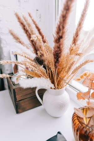 Vase with bouquet of dried spikelets and plants, home decorations on the windowsill.の写真素材