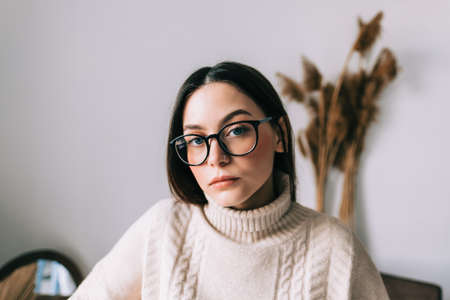 Authentic lifestyle portrait of pensive young caucasian woman in eyeglasses at home looking at camera.の写真素材