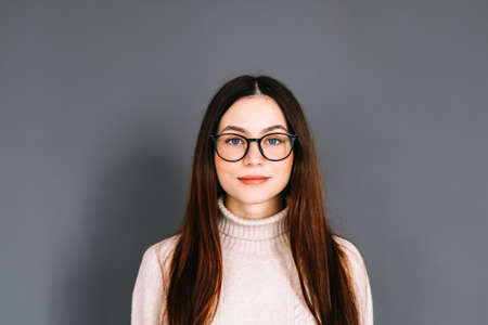Portrait of smiling young caucasian woman in eyeglasses on gray background looking at camera.