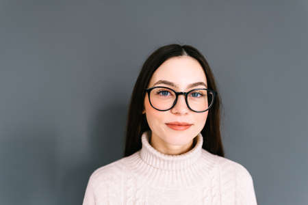 Portrait of smiling young caucasian woman in eyeglasses on gray background looking at camera.の写真素材