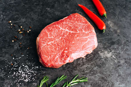 Raw beef steak on black background with rosemary, chili pepper and spices.の写真素材