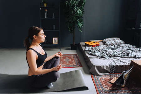 Young caucasian fitness woman meditate, doing yoga indoors at home near the bed. Staying fit and...