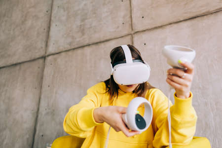 Young caucasian woman using VR headset, holding controllers and looking in virtual reality.