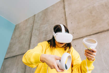 Young caucasian woman using VR headset, holding controllers and looking in virtual reality.