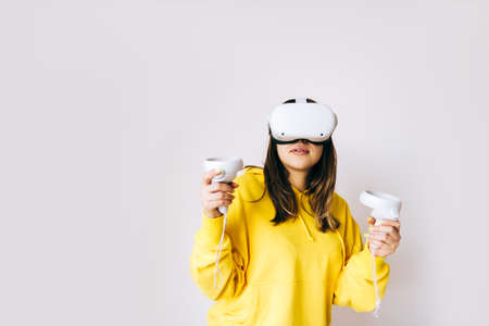 Young caucasian woman using VR headset, holding controllers and looking in virtual reality isolated on white background.の写真素材