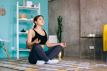 Young caucasian fitness woman meditate, doing yoga indoors at home near the bed. Staying fit and healthyの写真素材