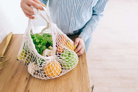 Caucasian woman hold eco net bag with fresh vegetables in modern kitchen.