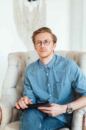 Portrait of serious caucasian man psychologist sitting in armchair at the workplace, holding a folder with papers for notes.の写真素材