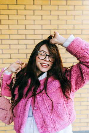 Portrait of young cheerful caucasian woman with brunette hair in eyeglasses and stylish clothing near brick wall outdoor.の写真素材