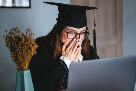Happy young caucasian woman celebrating college graduation during a video call with friend or family.の写真素材