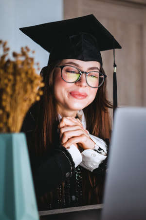 Happy young caucasian woman celebrating college graduation during a video call with friend or family.の写真素材