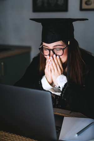Happy young caucasian woman celebrating college graduation during a video call with friend or family.の写真素材