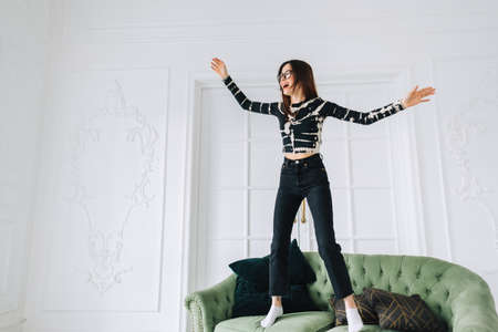 Young cheerful caucasian woman jumping on a sofa in living room.の写真素材