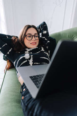 Attractivel young caucasian woman resting on a sofa and using laptop computer. Watching video, Chatting with friends, browsing informationの写真素材