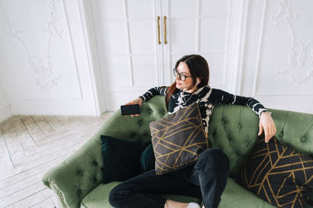 Attractive caucasian woman in earphones relaxing on comfortable sofa at home and listening music.