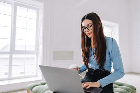 Attractive pretty young woman in eyeglasses freelancer using laptop computer at home, typing text...