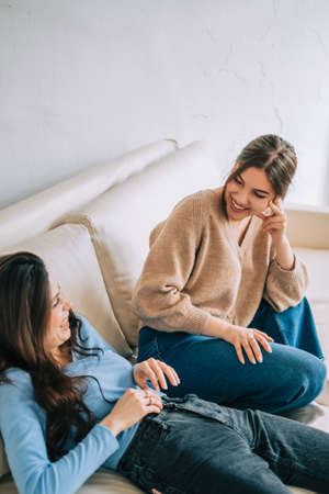 Two cheerful woman friend sitting on a sofa and talking with each other.の写真素材