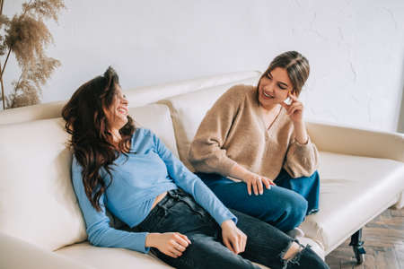 Two cheerful woman friend sitting on a sofa and talking with each other.の写真素材