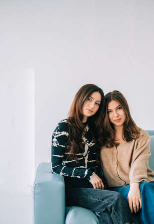 Portrait of two attractive stylish women sitting on blue sofa in white living room.の写真素材