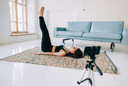 Beautiful brunette fitness woman make stretching exercises in front camera on tripod, doing yoga...