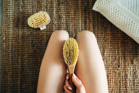 Woman holding wooden brush and doing dry massage on her feet. Self care concept